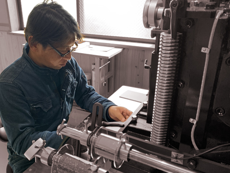 箔押印刷　Vamboo　代表でプリンティングアドバイザーの竹内智彦が箔押し機の前で作業をしています。